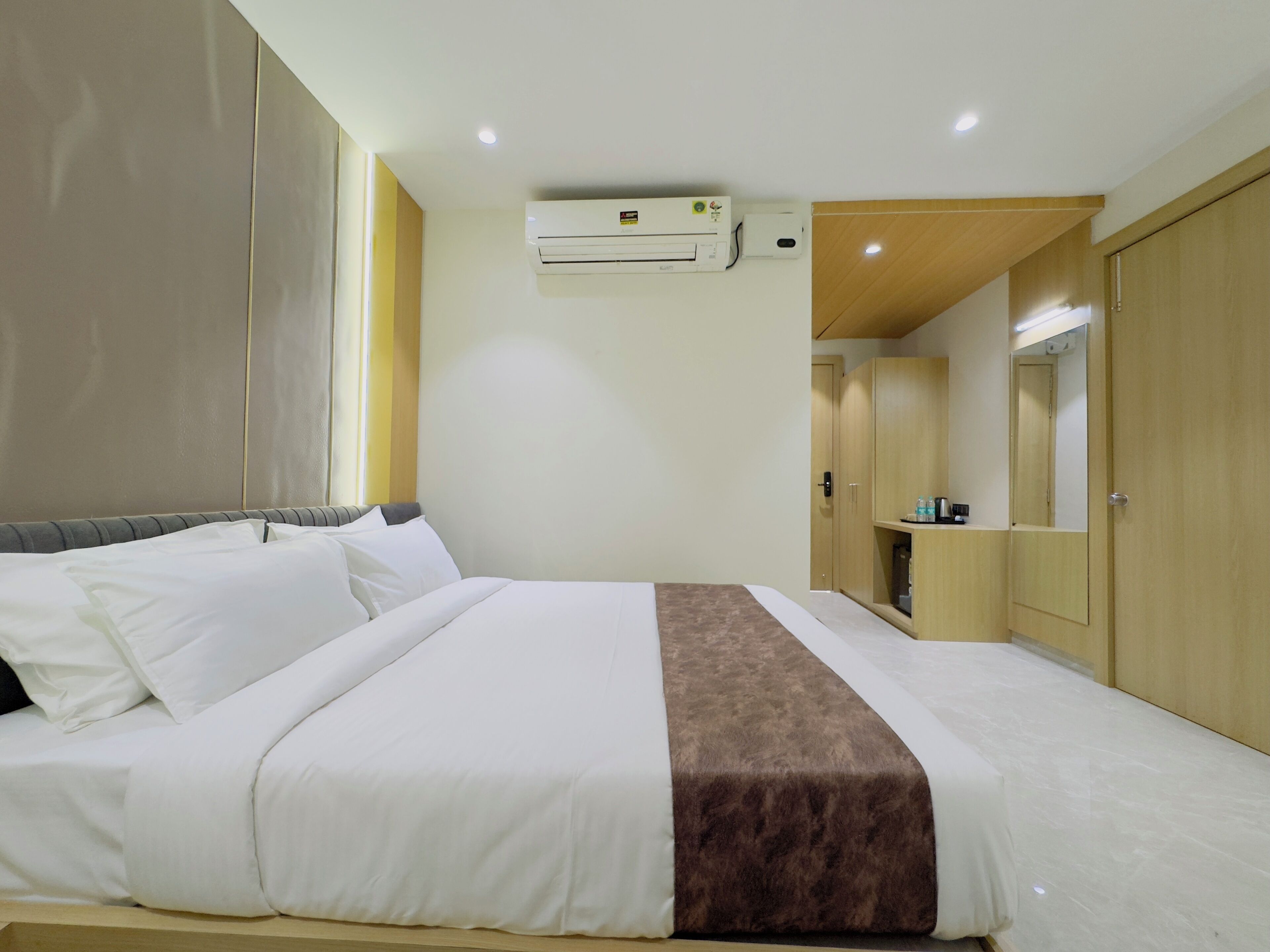 A hotel room with a bed, an air conditioning unit, a wardrobe, and a mirror.
