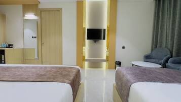 Habitación de hotel con dos camas, un televisor montado en la pared, una mesita y una silla.
