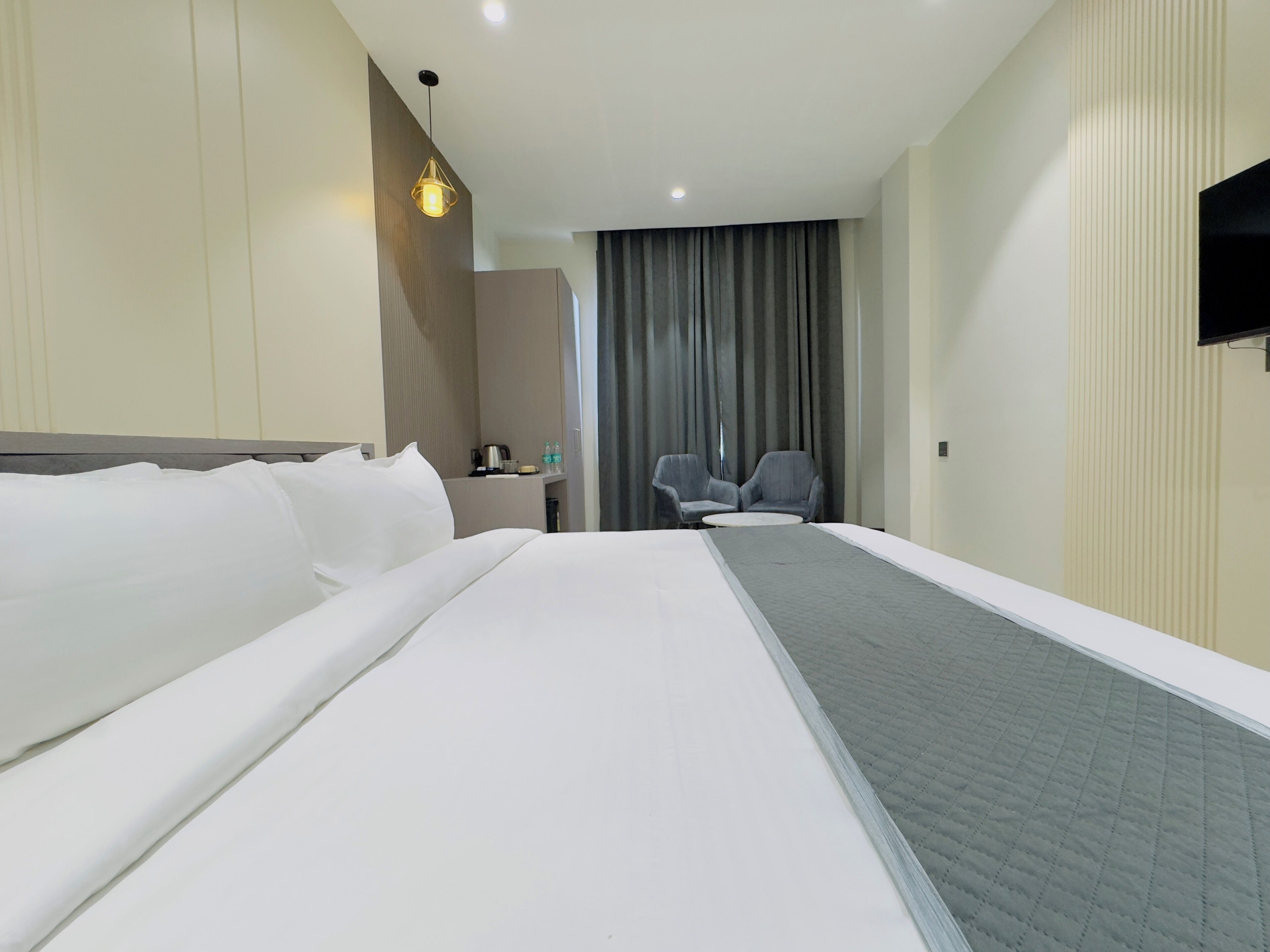 A hotel room with a large bed, a desk with a chair, a television, and a window with curtains.