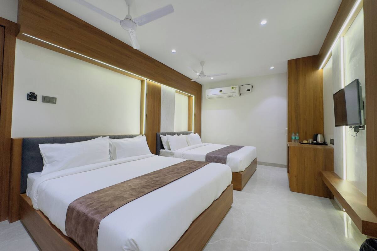 Une chambre d’hôtel avec deux lits, un ventilateur de plafond, un appareil de climatisation, un téléviseur fixé au mur et une petite table avec des articles de toilette.