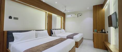 Une chambre d’hôtel avec deux lits, un ventilateur de plafond, un appareil de climatisation, un téléviseur fixé au mur et une petite table avec des articles de toilette.