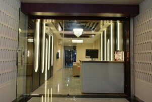 Un moderno hall de hotel con mostrador de recepción, una araña de cristal y un muro divisorio de vidrio.