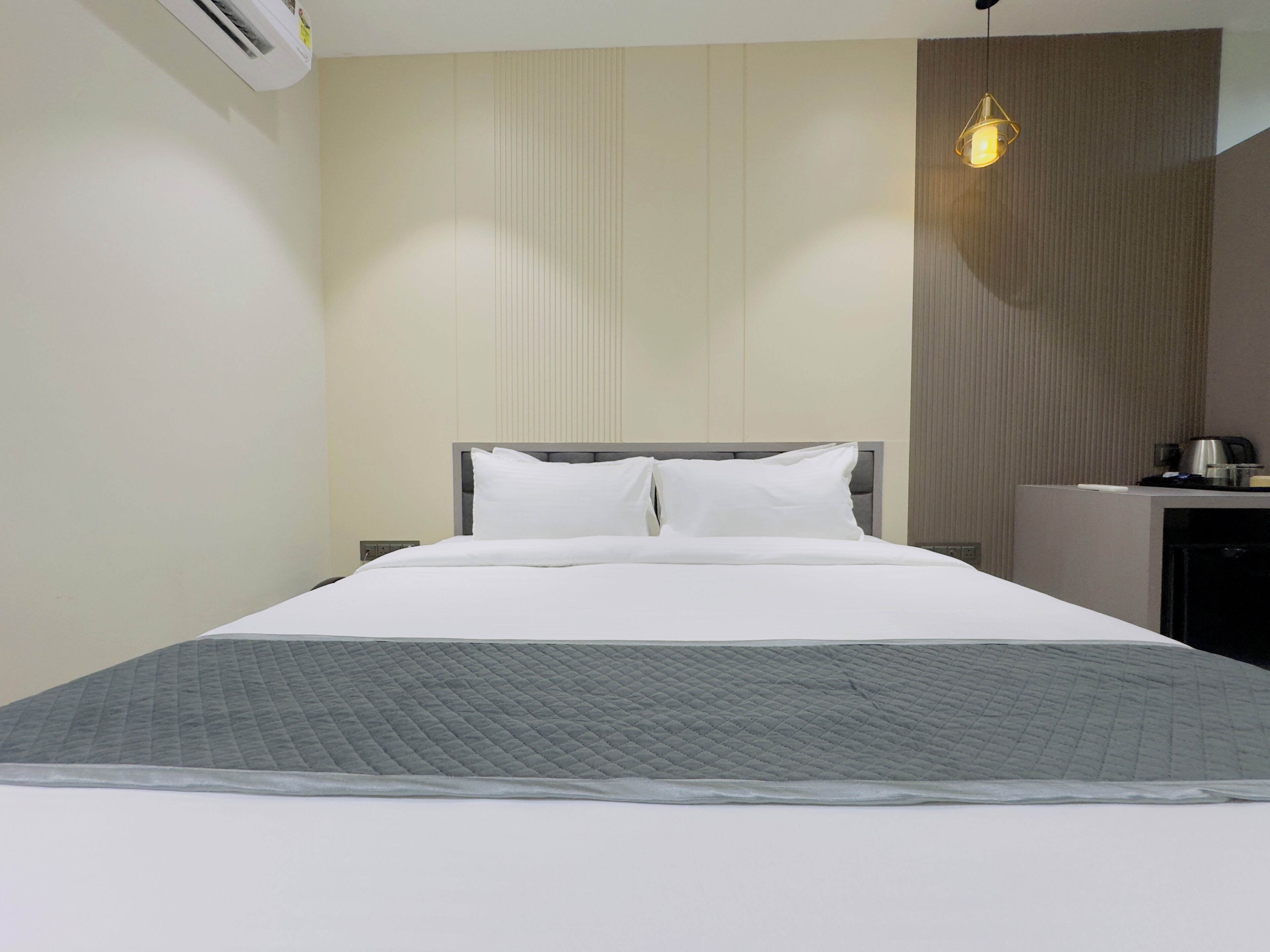 A hotel room with a bed, a bedside table, a lamp, and a wall-mounted air conditioner.