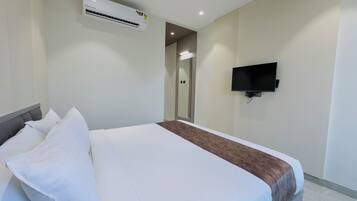 A hotel room with a bed, a flat-screen TV mounted on the wall, and an air conditioning unit above the bed.