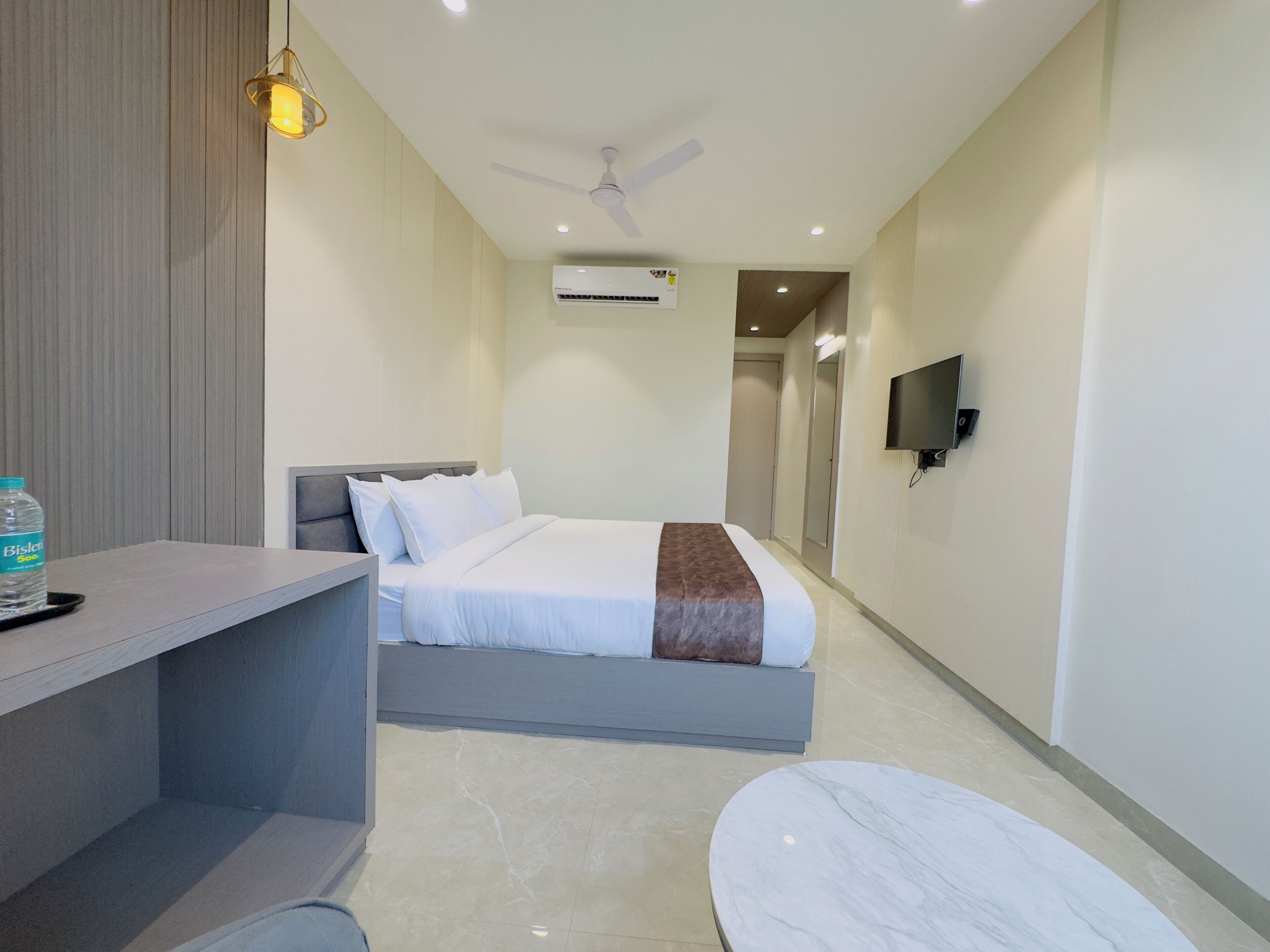 Una habitación de hotel moderna con cama, escritorio, silla, televisor y aire acondicionado.