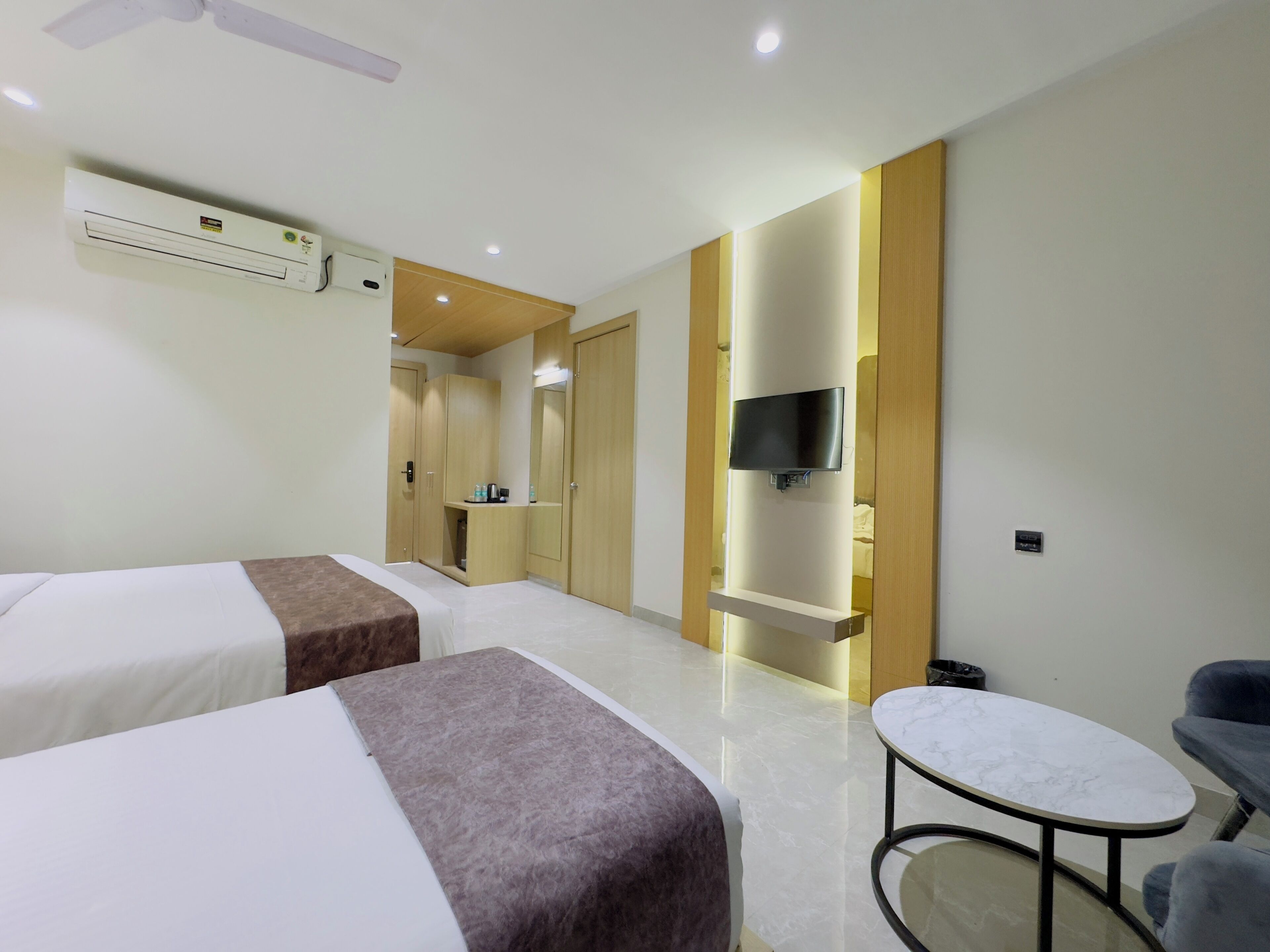 A hotel room with two beds, a TV mounted on the wall, a small table, and a chair.
