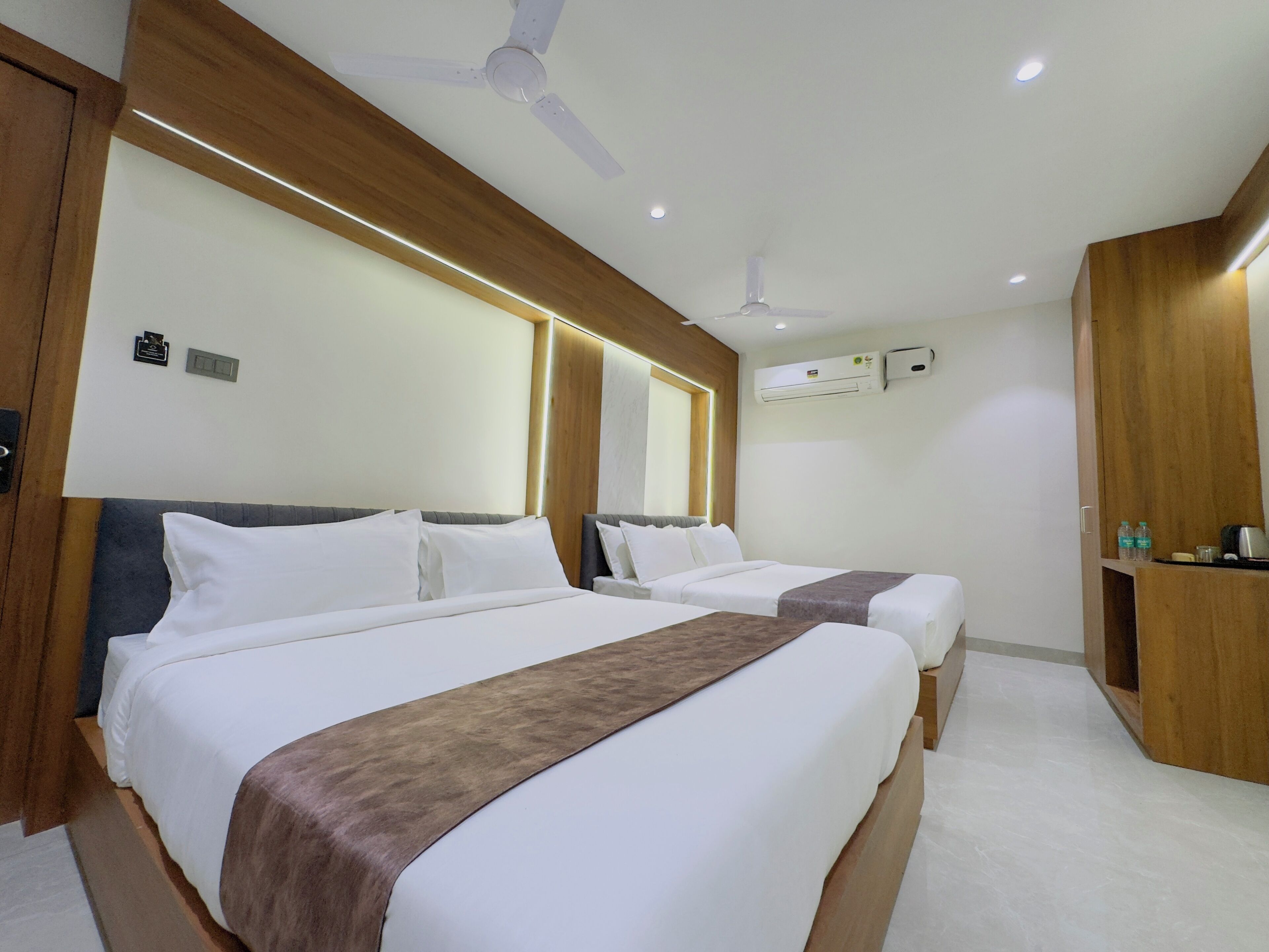 Ein Hotelzimmer mit zwei Betten, einem Deckenventilator, einer Klimaanlage und einem Holzschrank.