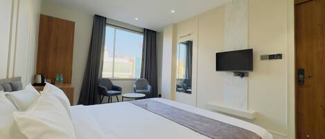 A hotel room with a large bed, two armchairs, a small table, a TV mounted on the wall, and a window with curtains.