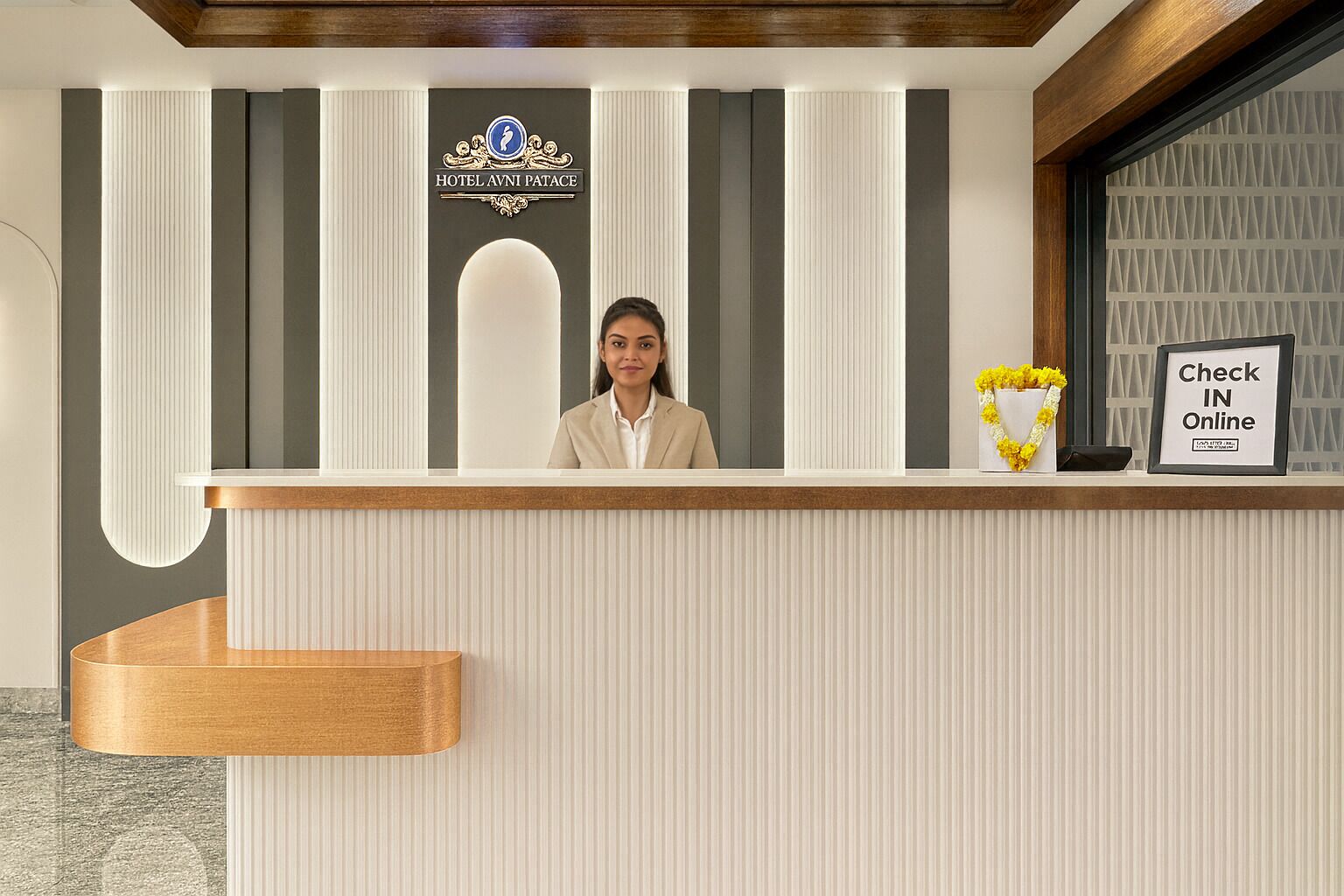 A hotel reception desk with a sign reading "Hotel Avni Palace," a "Check In Online" sign, and a vase with yellow flowers.