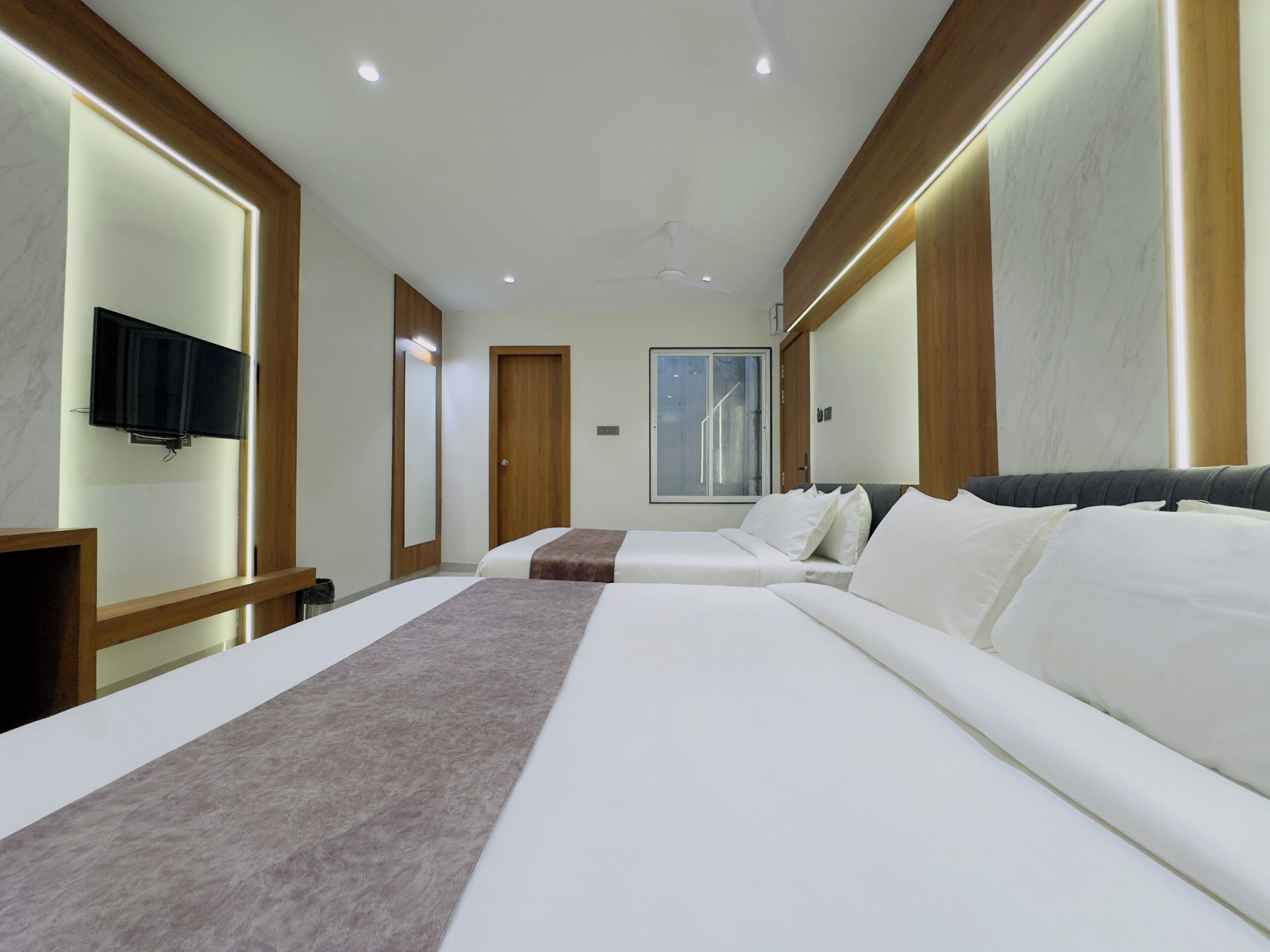 A hotel room with two beds, a TV, a large window, and wooden paneling.