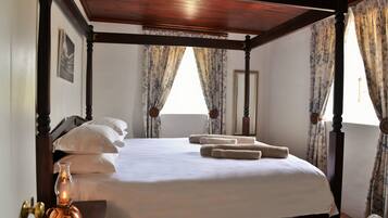 A four-poster bed with white linens and rolled towels, a brass door handle, and a lit candle on a wooden nightstand.