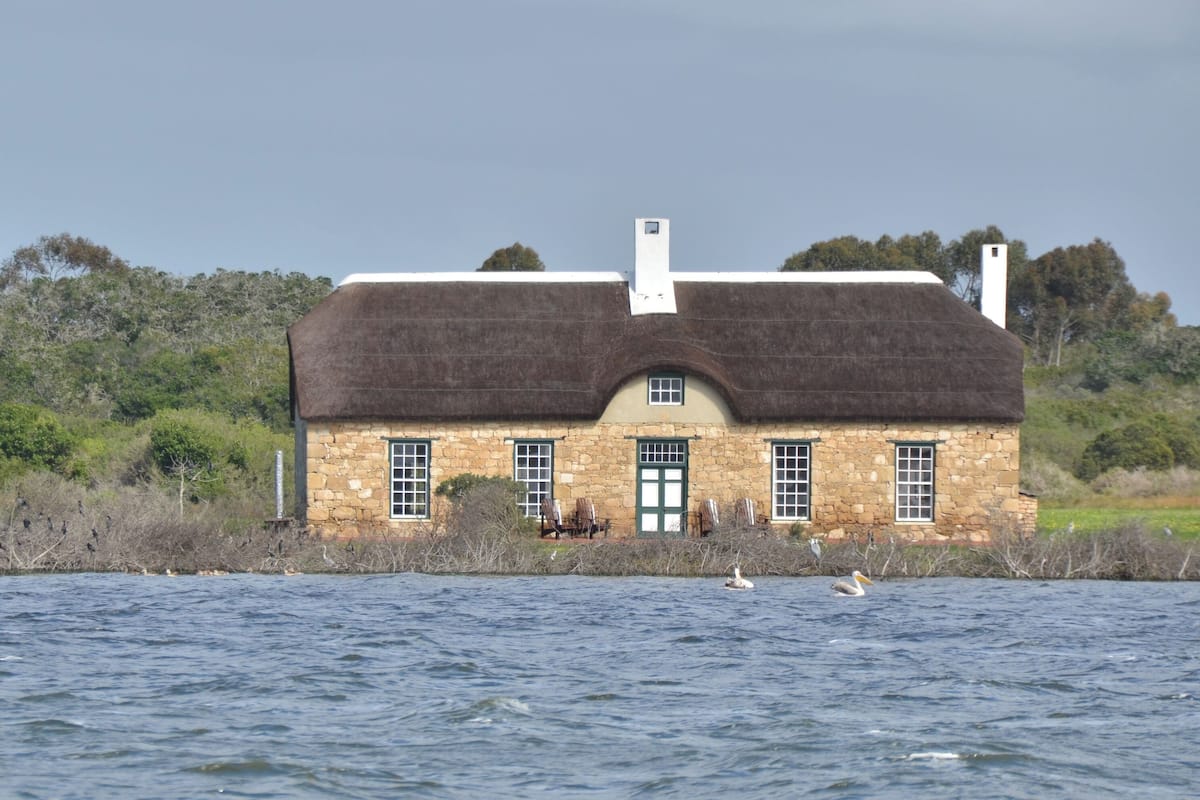 A stone house with a thatched roof by a body of water.