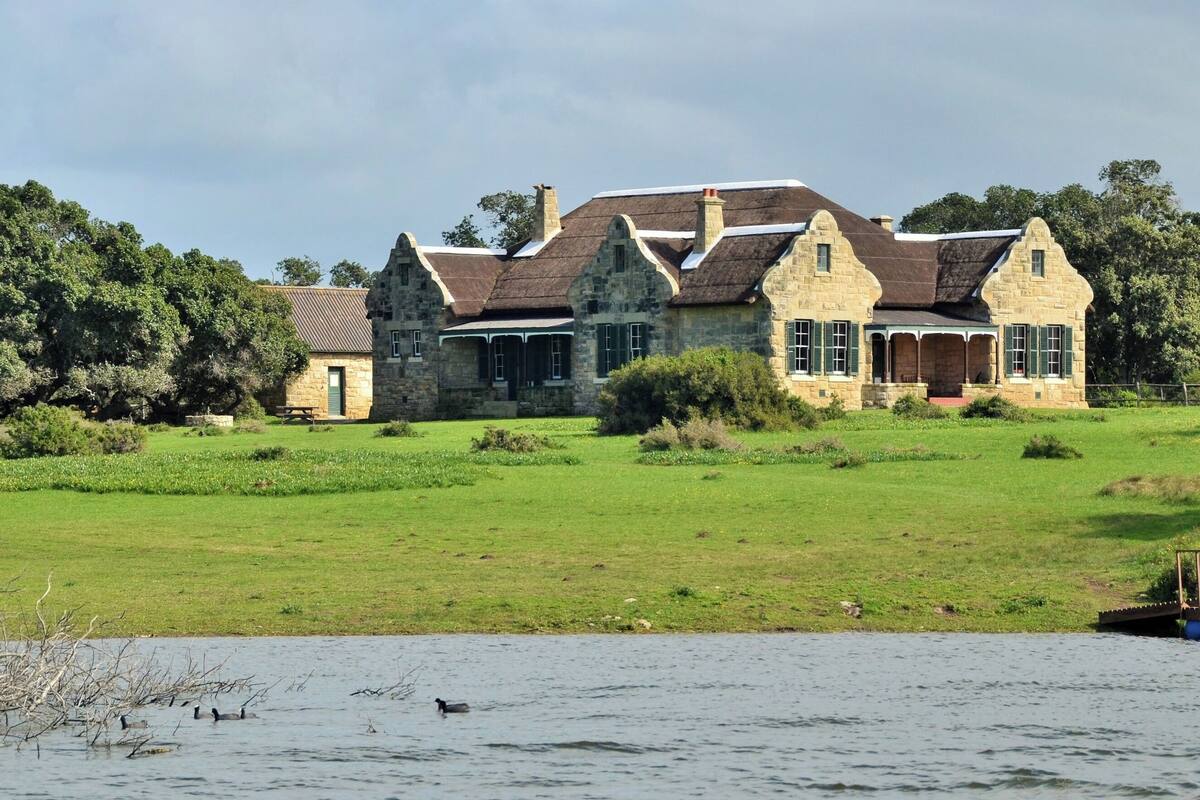 A stone house with a large lawn and a dock by a body of water.
