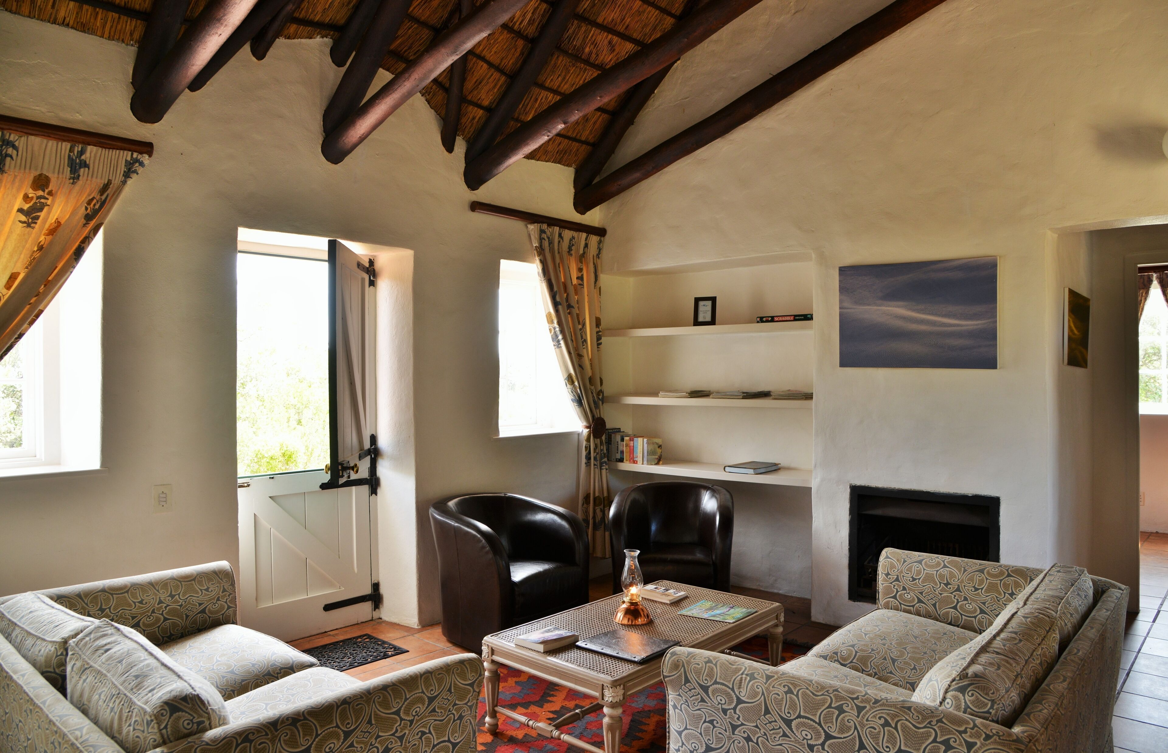 A cozy living room with a fireplace, leather chairs, patterned sofas, and a bookshelf.