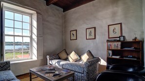 A living room with a sofa, chairs, a coffee table, and a bookshelf. There is a window with a view of the outdoors. - Melkkamer by De Hoop Collection (Overberg)