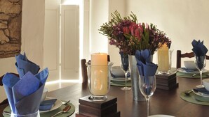 A dining table set with glassware, napkins, and a candle, with a stone wall and wooden ceiling in the background. - Melkkamer by De Hoop Collection (Overberg)