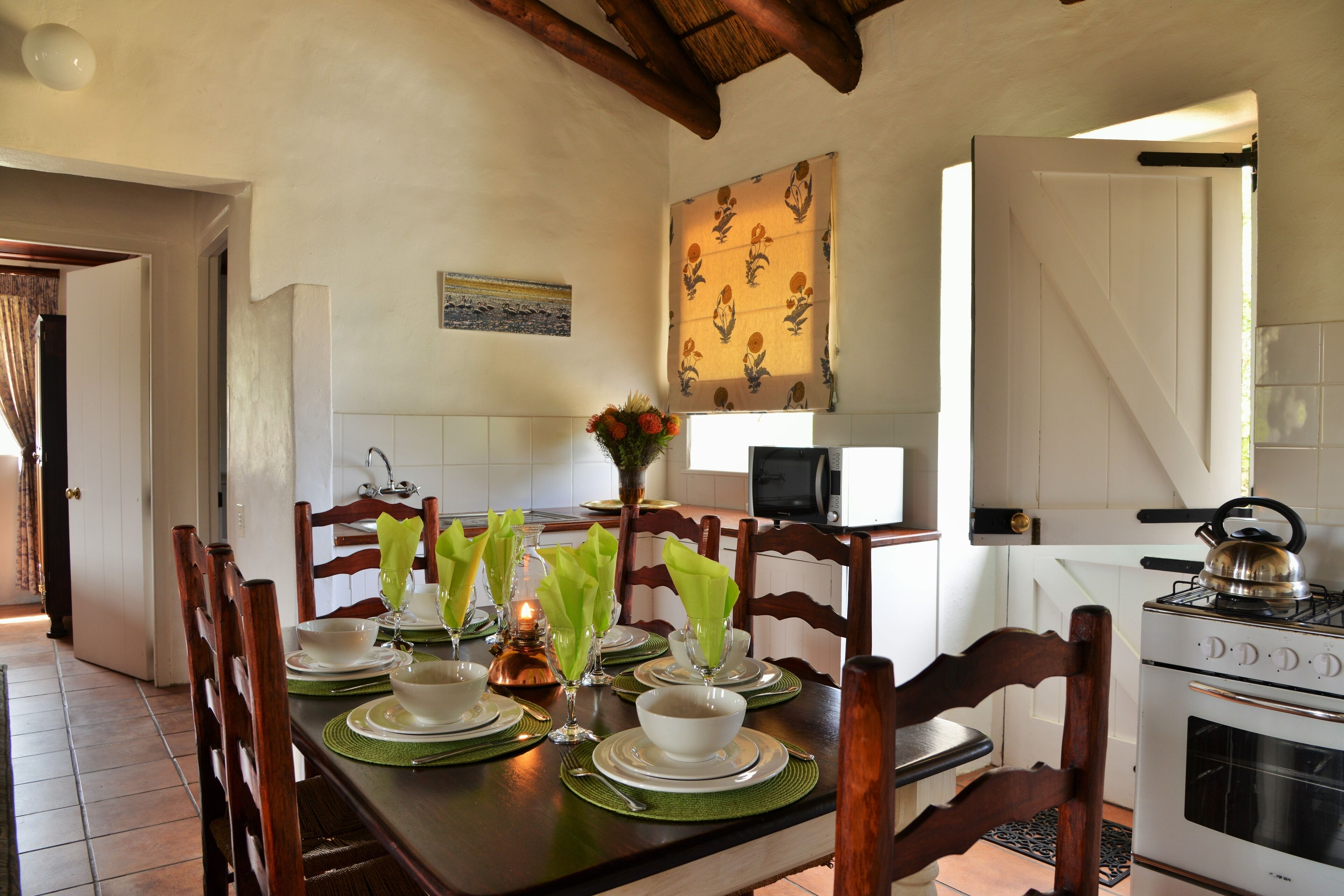 Un comedor con una mesa de madera dispuesta para cuatro personas, individuales verdes, platos blancos y un jarrón con flores.