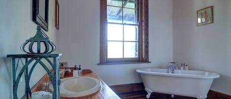 Un baño con tocador de madera, un lavamanos blanco, una bañera independiente y una ventana con vistas al exterior.