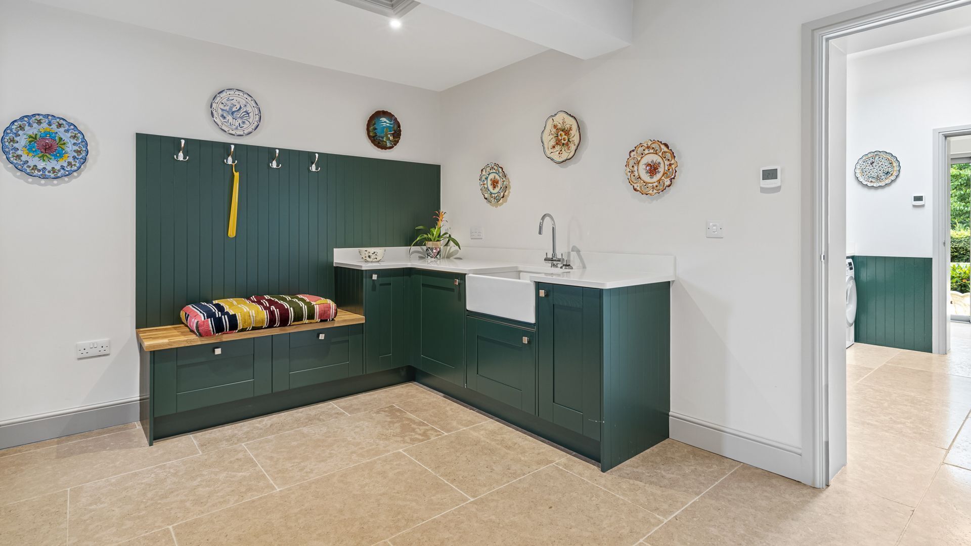 A modern kitchen with dark green cabinets, a white countertop, and a built-in sink. There are decorative plates on the wall and a colorful rug on the floor.