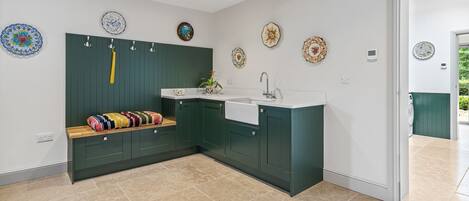 A modern kitchen with dark green cabinets, a white countertop, and a built-in sink. There are decorative plates on the wall and a colorful rug on the floor.