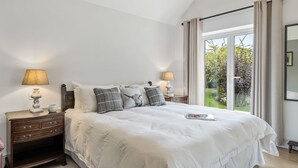 Une chambre avec un grand lit, deux tables de chevet avec des lampes, une petite table et une vue sur la verdure grâce à une porte-fenêtre coulissante.