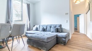 Un salon moderne avec un canapé d’angle, une table à manger avec des chaises et une grande fenêtre agrémentée de rideaux.