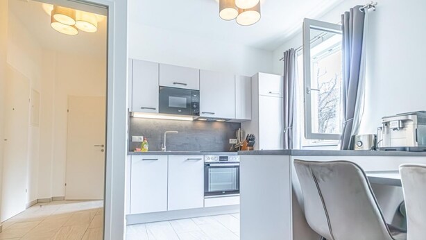 Une cuisine moderne avec des meubles blancs, un four à micro-ondes, un four traditionnel et un coin repas avec une chaise.