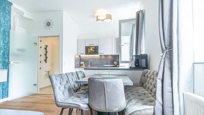 Une cuisine moderne dotée d’un îlot central, d’un coin repas avec une table et des chaises, et d’une porte visible donnant sur une autre pièce.