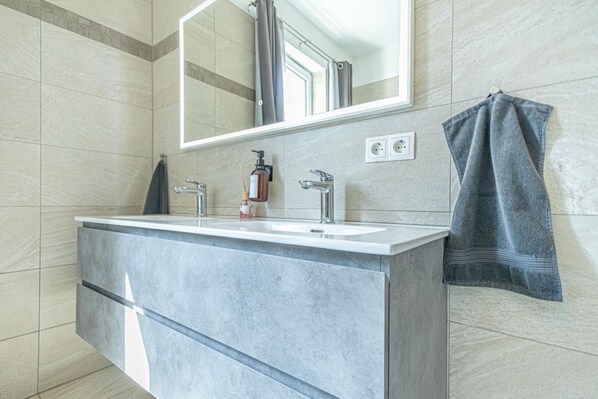 A bathroom with a large mirror, two sinks, a towel rack, and a bottle of soap.