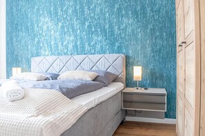 Une chambre à coucher avec un lit, des tables de chevet et un mur orné d’un motif bleu texturé.