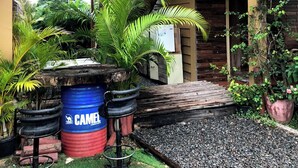 En bygning med balkon, en blå tønde med teksten "CAMEL" og forskellige planter.