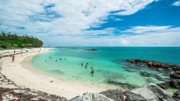 Una playa con aguas turquesas cristalinas, una orilla arenosa y afloramientos rocosos.