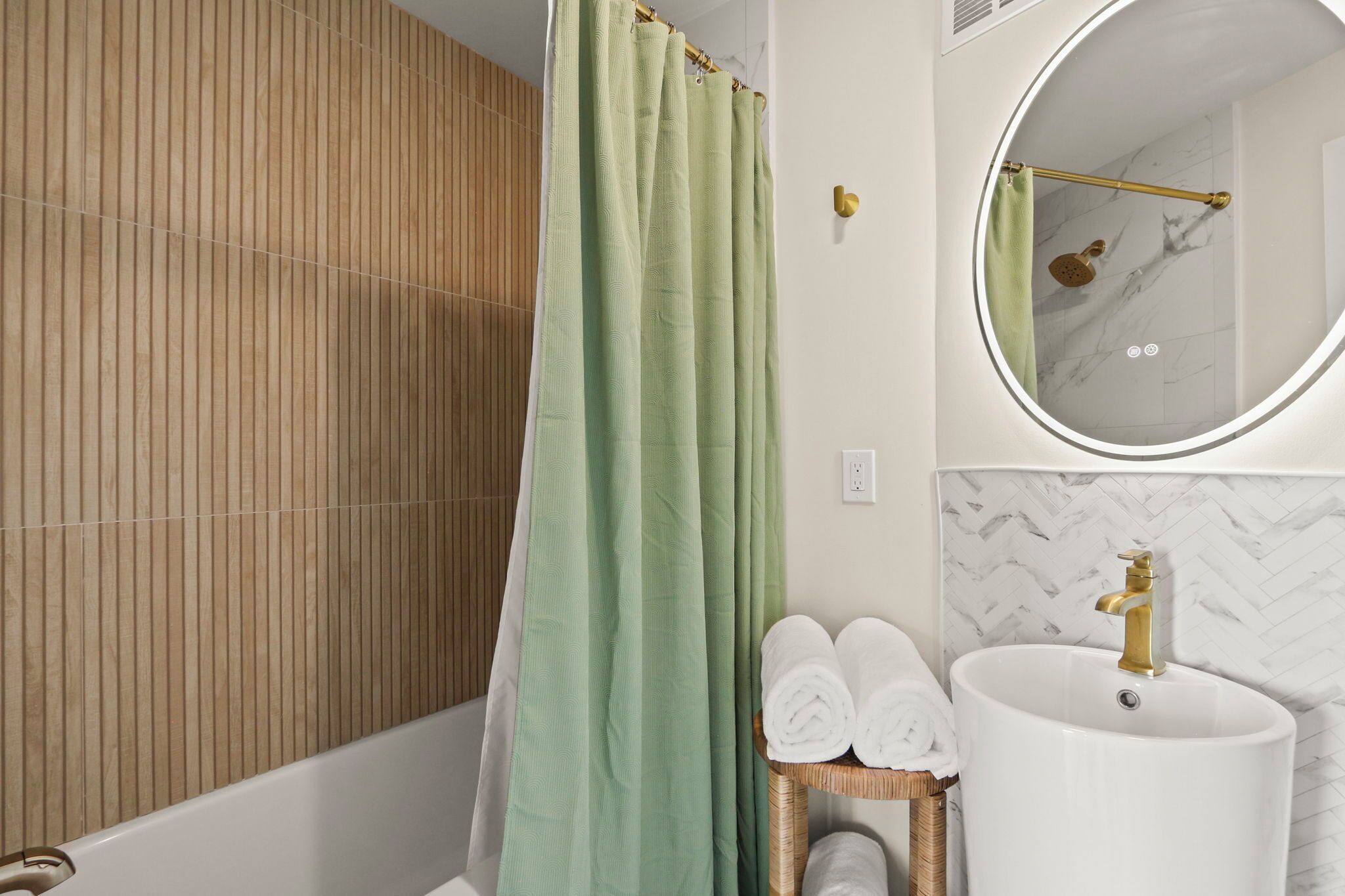 A bathroom with a green shower curtain, a white sink with a gold faucet, and a mirror with a gold frame.