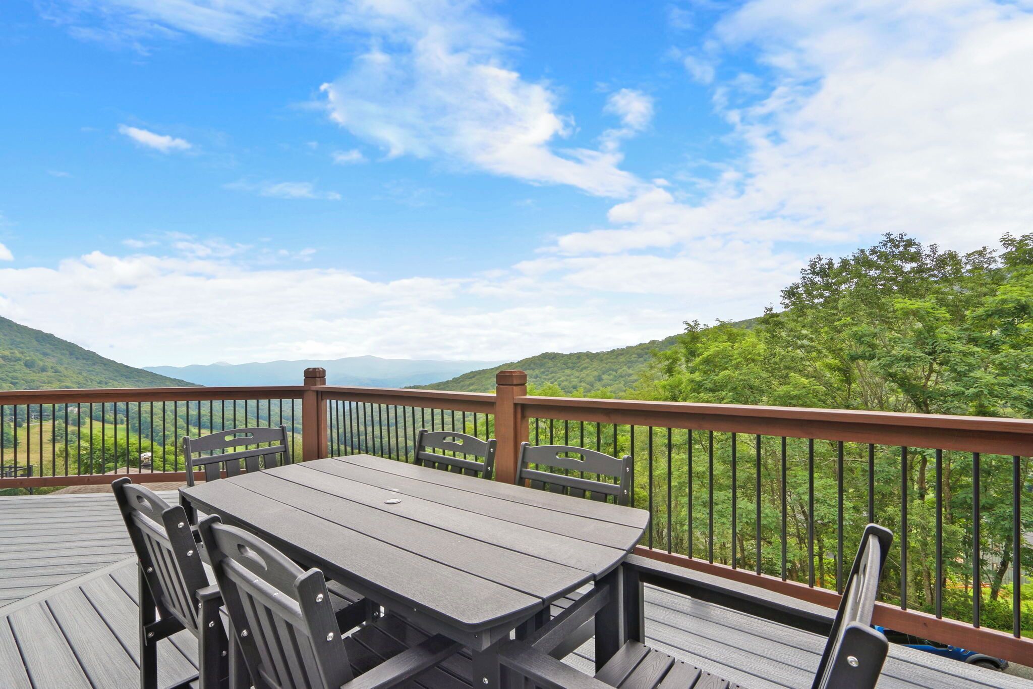 Une terrasse en bois avec une table et des chaises, offrant une vue sur un paysage montagneux.