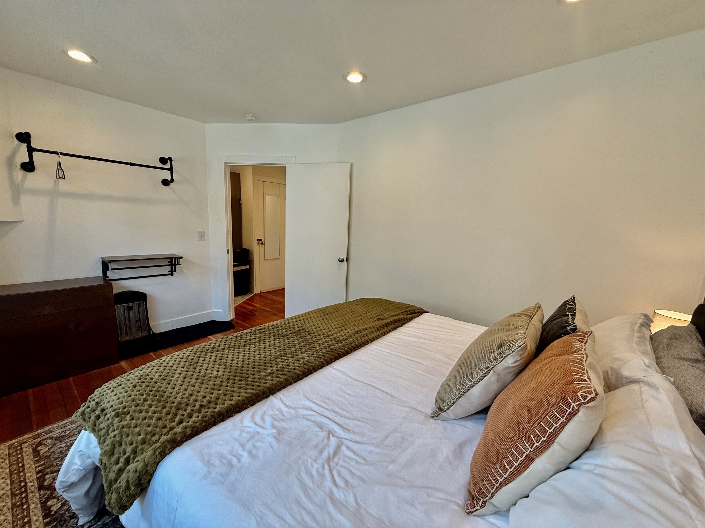 Une chambre à coucher comprenant un lit, des oreillers, une table de chevet, une armoire et une porte donnant sur une autre pièce.