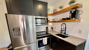 Een moderne keuken met roestvrijstalen apparatuur, donkere kastjes en een houten plank met planten.