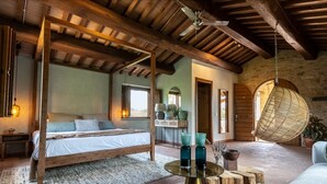 A rustic bedroom with a wooden bed, a hanging chair, and a round table with decorative items. - Borgo Castello Panicaglia (Nocera Umbra)
