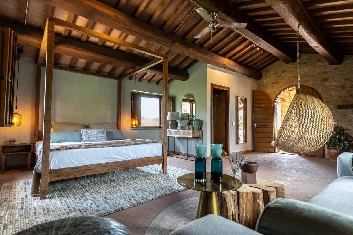 Un dormitorio rústico con una cama de madera, una silla colgante y una mesa redonda con objetos decorativos.