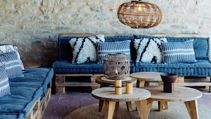 A rustic room with a stone wall, wooden beams, a blue sofa with patterned cushions, and a woven light fixture. - Borgo Castello Panicaglia (Nocera Umbra)