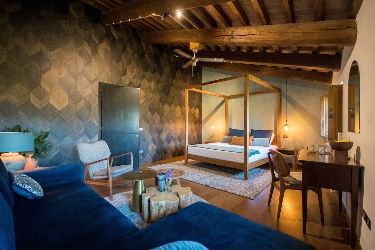 Un dormitorio con cama con dosel, una zona de estar con sofá y sillones, una mesa de comedor y un ventilador de techo.