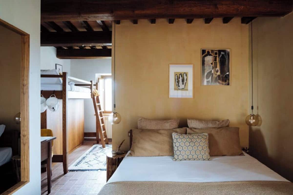 Un dormitorio con una cama doble, una escalera de madera, una cama con múltiples almohadas y dos lámparas fijadas a la pared.
