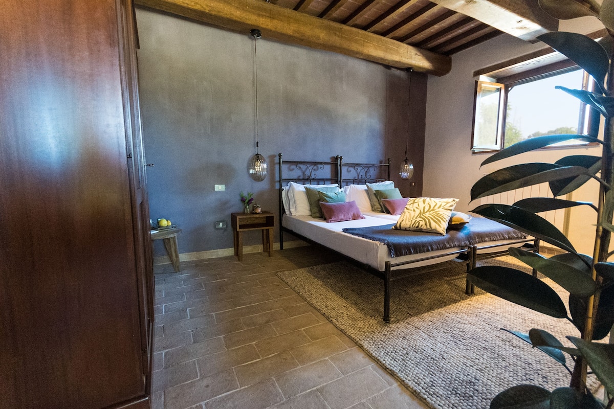Un dormitorio con cama, mesita de noche, planta en maceta y ventana.