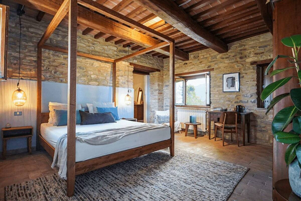 Un dormitorio rústico con cama con dosel, paredes de piedra, vigas de madera, chimenea de piedra y un ventanal grande.