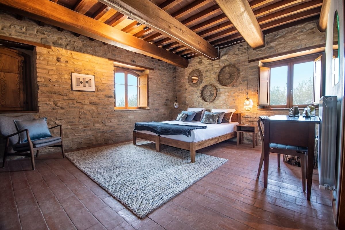 Un dormitorio rústico con pared de piedra, vigas de madera, cama, escritorio y silla.