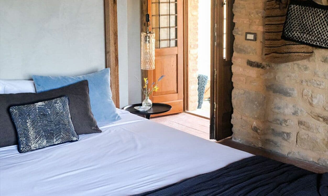 Un dormitorio con una cama grande, una mesita con un florero y una puerta de madera que da al exterior.