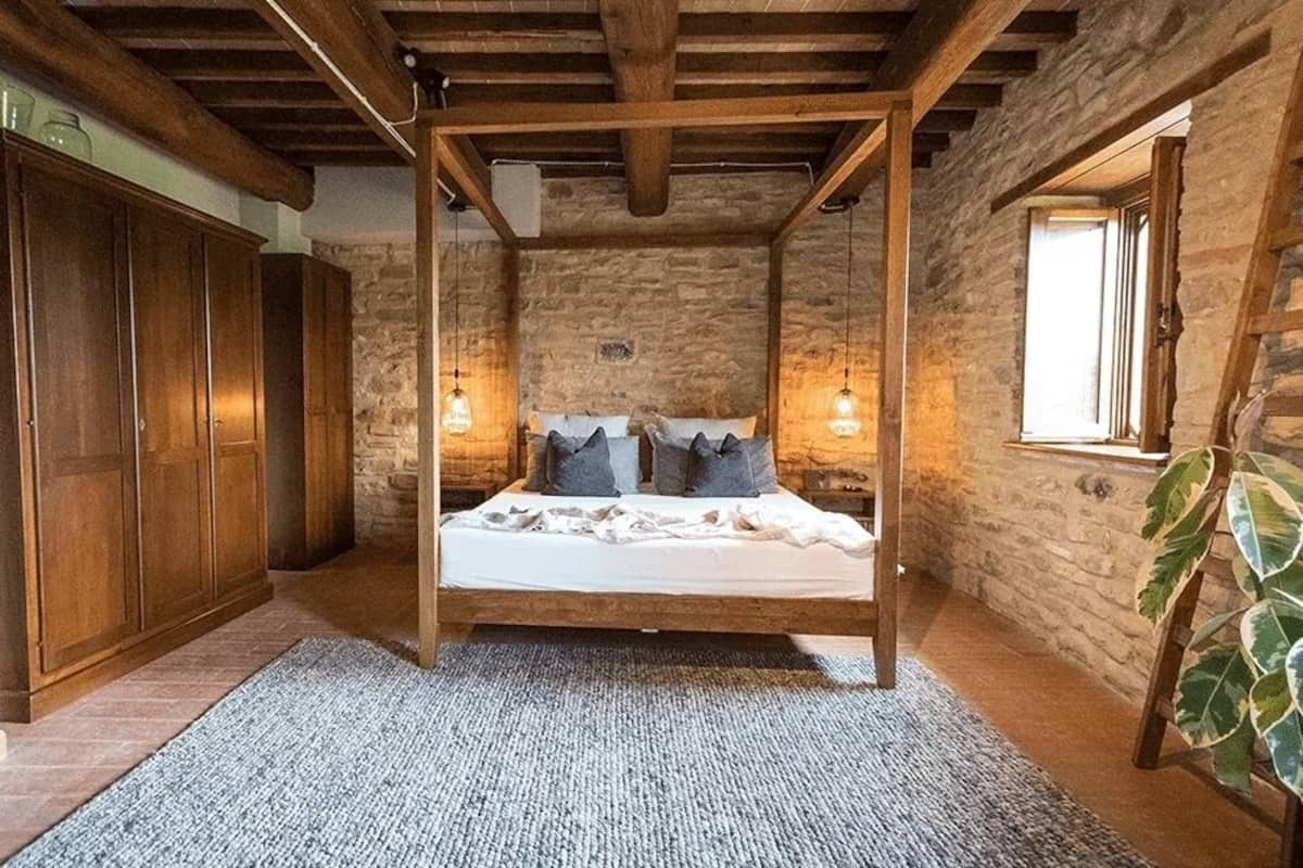 Un dormitorio con cama con dosel, armario de madera, paredes de piedra y un ventanal grande.