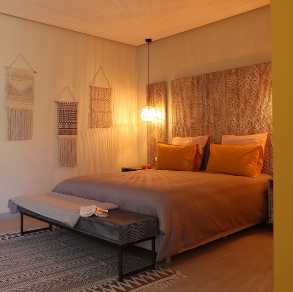 A bedroom with a large bed, a bedside table, a hanging light fixture, and patterned wall hangings. - YMY BEACH HOUSE (Tamri)