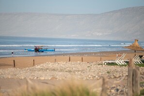 A beach with a boat, beach chairs, and a thatched structure. - YMY BEACH HOUSE (Tamri)