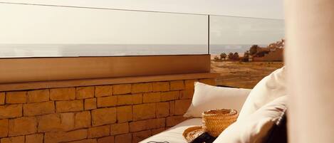 Un balcón con vista al mar, un muro de ladrillo y una silla de mimbre con cojines.