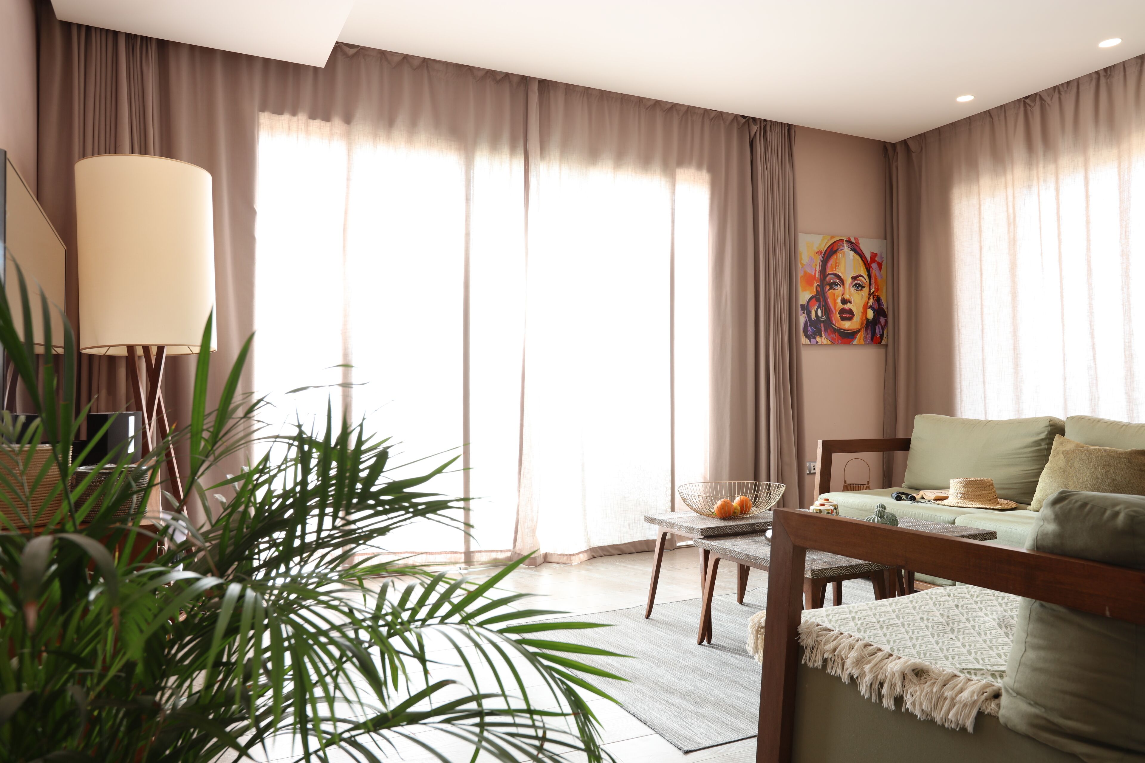 A well-lit room with a bed, a dining table, and a large window with curtains.